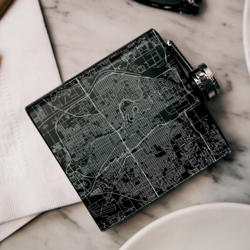 Matte black hip flask featuring a custom engraved map of Wichita, Kansas with coordinates, accompanied by a canvas bag and funnel.